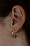 Small gold hoop earrings with geometric linear design, worn on an ear, 14k delicate jewelry