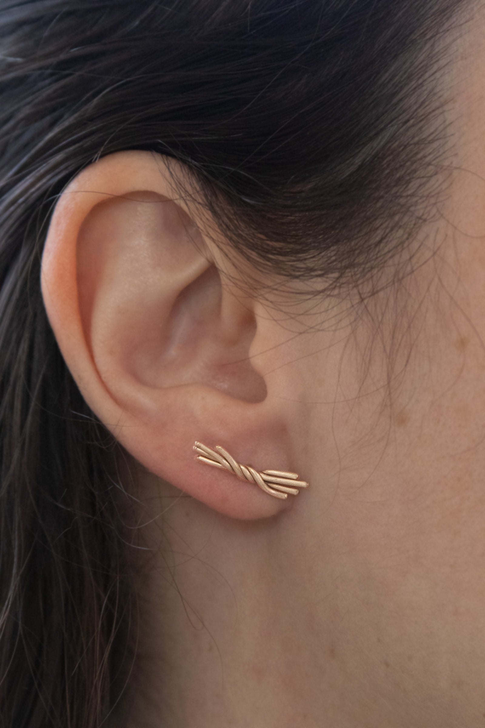 14K gold studs in a brushed finish with twisted wires, closeup on ear